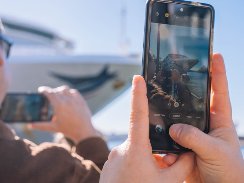 Hands holding an Iphone to take a photo of a boat